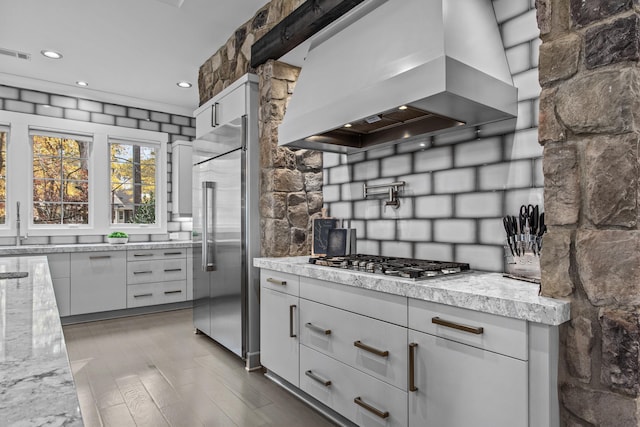 1031 Fish Trap Shls, Greensboro, GA 30642 - kitchen with wall chimney range hood, appliances with stainless steel finishes, wood finished floors, light stone countertops, and tasteful backsplash