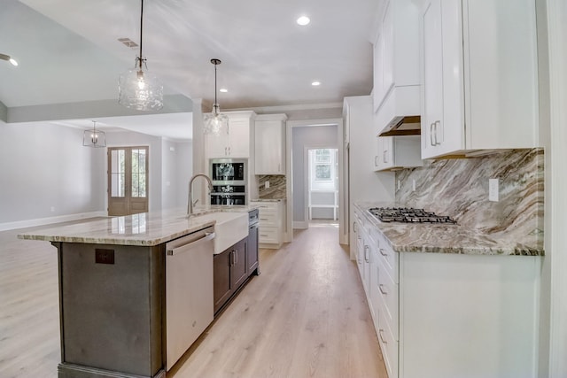 kitchen featuring appliances with stainless steel finishes, white cabinetry, decorative light fixtures, a large island with sink, and light wood-type flooring