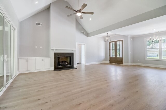 unfurnished living room featuring ceiling fan with notable chandelier, light hardwood / wood-style flooring, high vaulted ceiling, and french doors