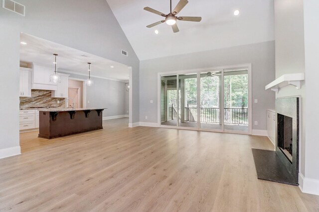 living room featuring sink, high vaulted ceiling, ceiling fan, a fireplace, and light hardwood / wood-style floors