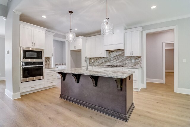 kitchen featuring white cabinetry, light stone counters, decorative light fixtures, a center island with sink, and stainless steel appliances