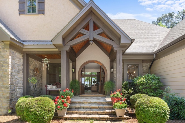entrance to property featuring stone siding, a porch, stucco siding, and a shingled roof