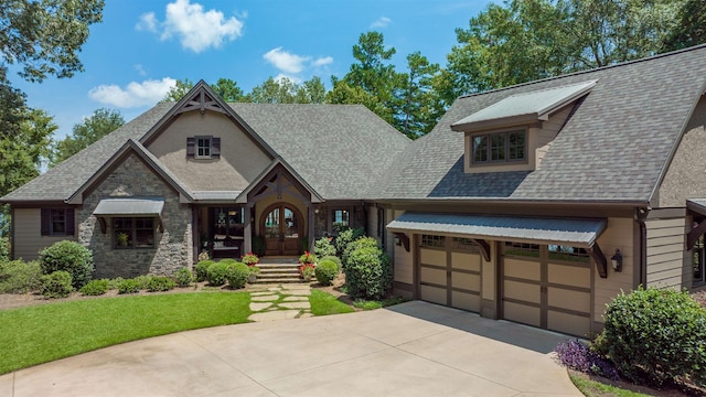 tudor-style house featuring stone siding, a shingled roof, an attached garage, and driveway