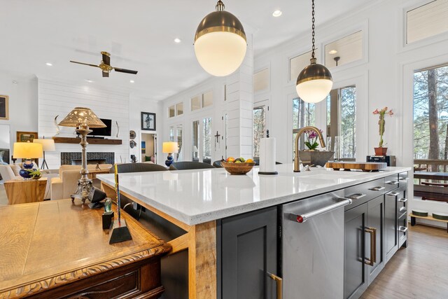 kitchen featuring light stone counters, hanging light fixtures, dishwasher, an island with sink, and a fireplace