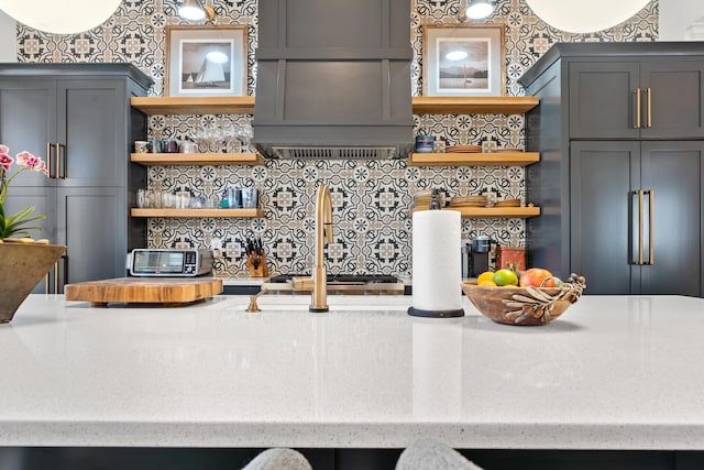 kitchen with light stone countertops, custom range hood, gray cabinetry, and decorative backsplash