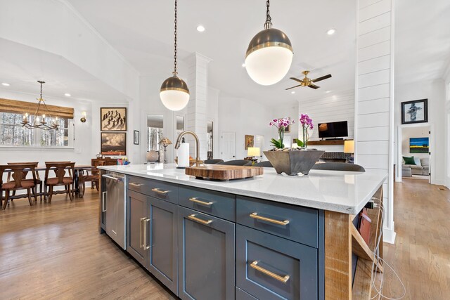 kitchen with ceiling fan, a kitchen island with sink, light stone countertops, light hardwood / wood-style floors, and decorative light fixtures