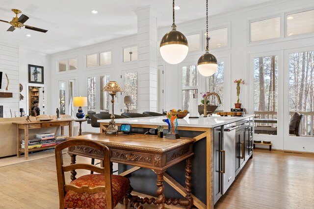 interior space featuring decorative light fixtures, sink, light hardwood / wood-style floors, plenty of natural light, and a center island with sink