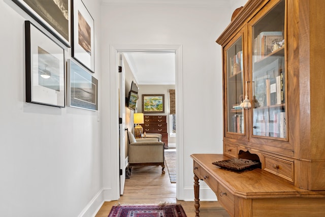 hallway with ornamental molding and light hardwood / wood-style flooring