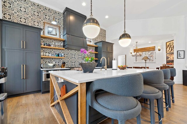 kitchen featuring pendant lighting, light hardwood / wood-style flooring, a kitchen island with sink, ornamental molding, and custom exhaust hood