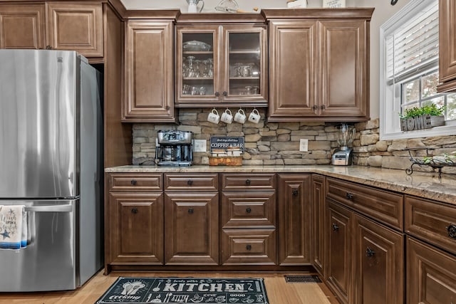 kitchen featuring light stone counters, stainless steel fridge, light hardwood / wood-style flooring, and backsplash