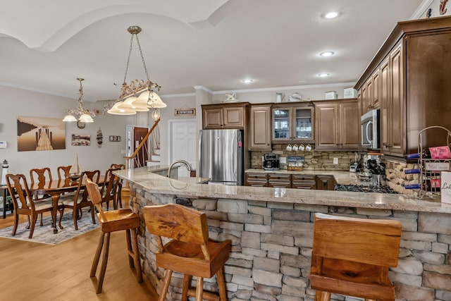 kitchen featuring decorative backsplash, hanging light fixtures, light stone counters, kitchen peninsula, and stainless steel appliances