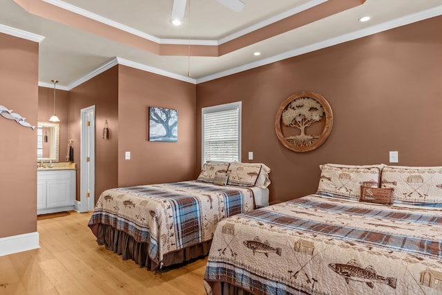 bedroom featuring connected bathroom, ornamental molding, ceiling fan, a tray ceiling, and light wood-type flooring
