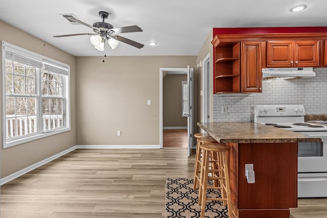 kitchen with a breakfast bar area, ceiling fan, white electric range oven, tasteful backsplash, and light hardwood / wood-style floors