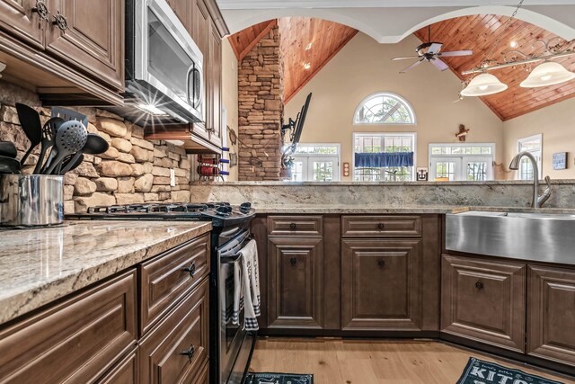 kitchen featuring stainless steel appliances, light stone countertops, dark brown cabinets, and sink