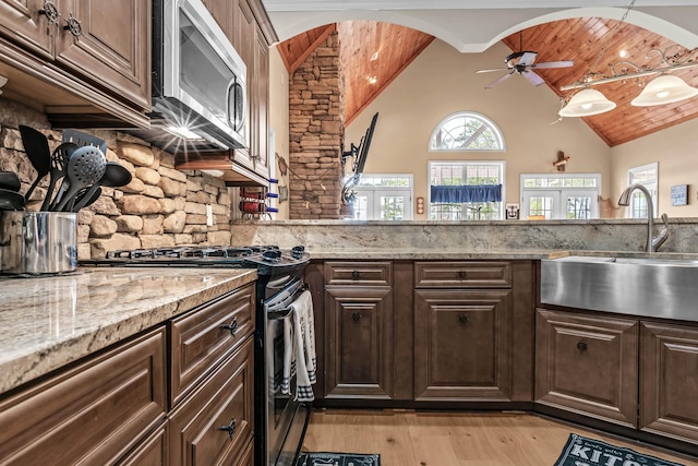 kitchen featuring stainless steel appliances, light stone countertops, dark brown cabinets, and sink