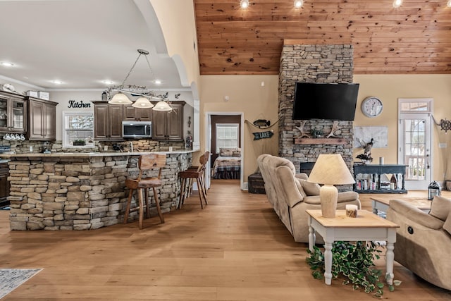 living room featuring crown molding, high vaulted ceiling, a fireplace, light hardwood / wood-style floors, and wooden ceiling