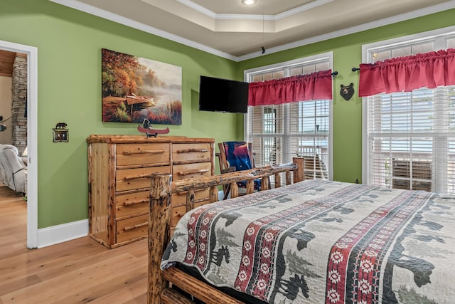 bedroom with ornamental molding, a raised ceiling, and light hardwood / wood-style flooring