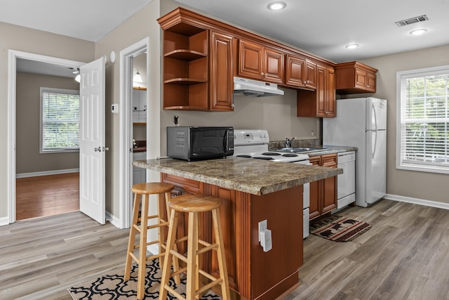 163 Knight Dr, Milledgeville, GA 31061 - kitchen with white appliances, under cabinet range hood, light wood-style floors, brown cabinetry, and a breakfast bar area