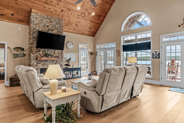 living room featuring a stone fireplace, wood ceiling, light wood-type flooring, and french doors