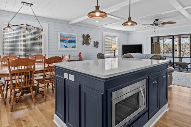 kitchen featuring stainless steel microwave, decorative light fixtures, light hardwood / wood-style floors, and a kitchen island