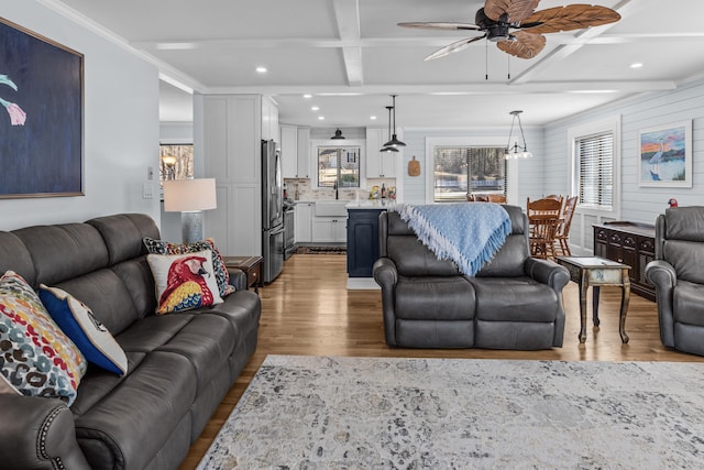 living room featuring ceiling fan with notable chandelier, beamed ceiling, wood-type flooring, ornamental molding, and coffered ceiling