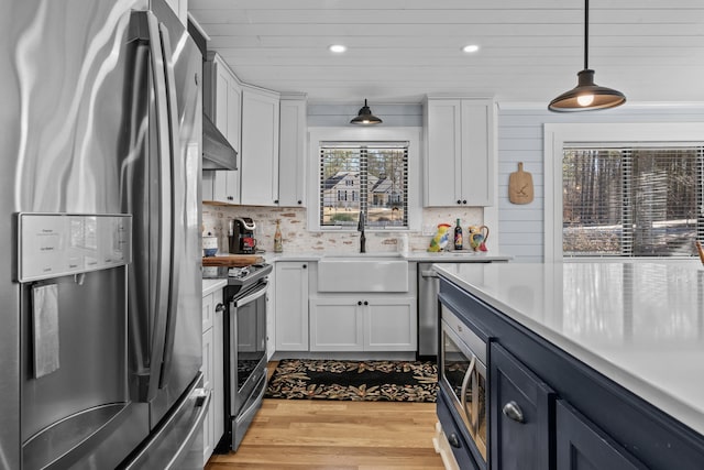 kitchen with appliances with stainless steel finishes, sink, pendant lighting, and white cabinets