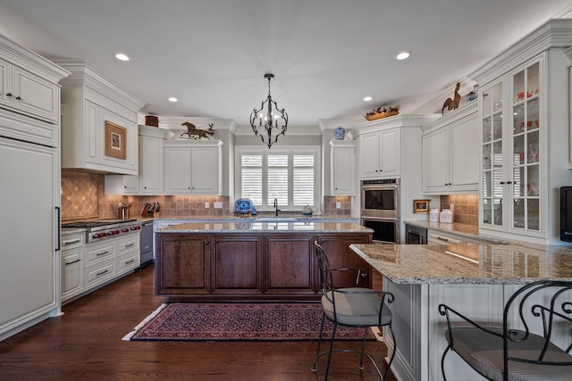 kitchen with sink, light stone counters, hanging light fixtures, appliances with stainless steel finishes, and white cabinets