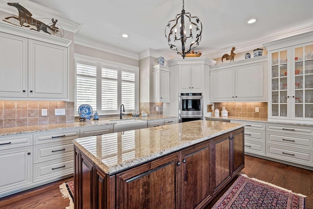 kitchen with sink, white cabinetry, hanging light fixtures, a kitchen island, and stainless steel double oven