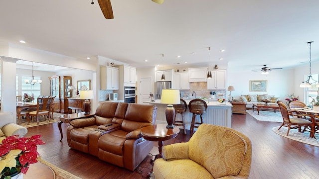 living room with sink, ornamental molding, dark hardwood / wood-style flooring, and ceiling fan with notable chandelier