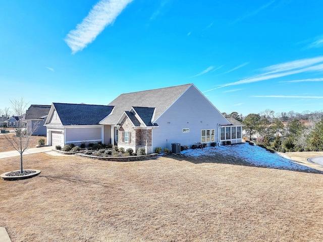 view of front of home with a garage, a sunroom, a front lawn, and central air condition unit