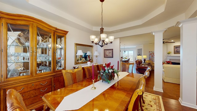 dining space featuring an inviting chandelier, a tray ceiling, dark wood-type flooring, and decorative columns