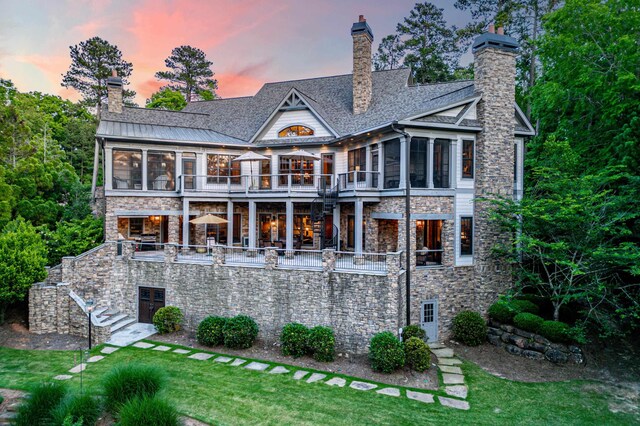 back house at dusk with a yard, a sunroom, and a balcony