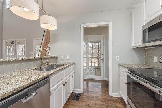 kitchen with light stone countertops, decorative backsplash, white cabinets, stainless steel appliances, and a sink