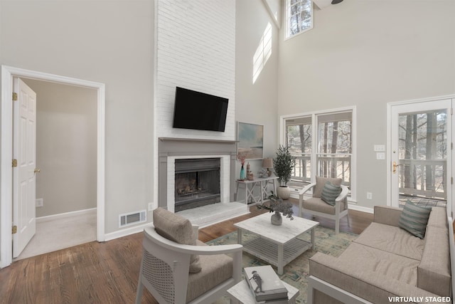 living room featuring visible vents, wood finished floors, baseboards, and a fireplace with raised hearth