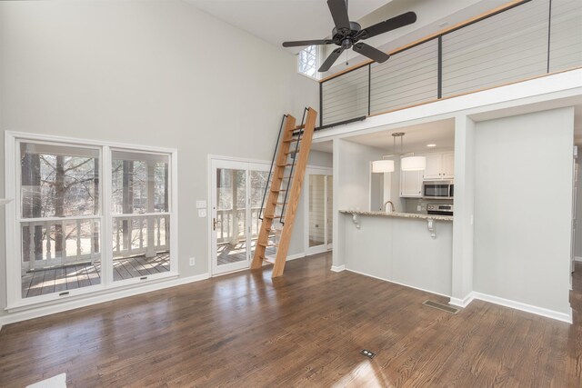 unfurnished living room with ceiling fan, baseboards, a high ceiling, and dark wood-style floors