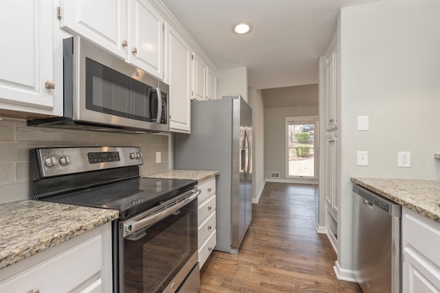 kitchen with wood finished floors, baseboards, white cabinets, appliances with stainless steel finishes, and tasteful backsplash