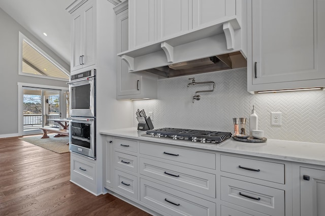 kitchen with appliances with stainless steel finishes, dark wood-style flooring, wall chimney exhaust hood, and tasteful backsplash