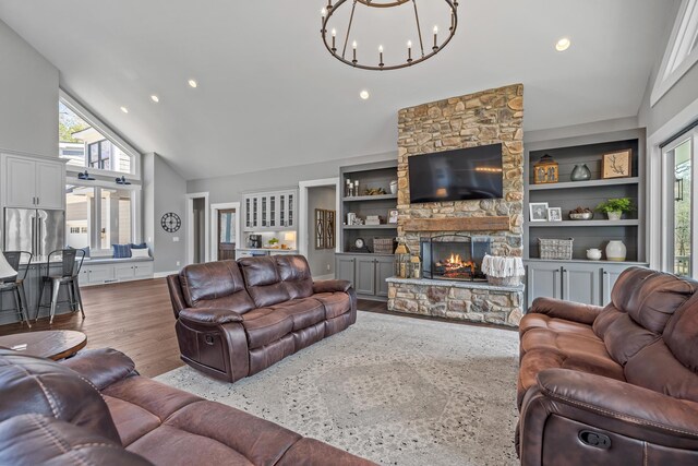 living area featuring high vaulted ceiling, a stone fireplace, built in shelves, recessed lighting, and wood finished floors