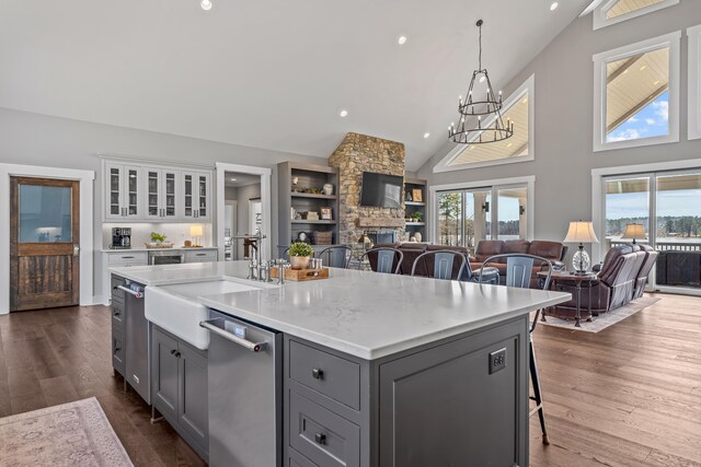 kitchen featuring open floor plan, gray cabinets, stainless steel dishwasher, a fireplace, and a sink