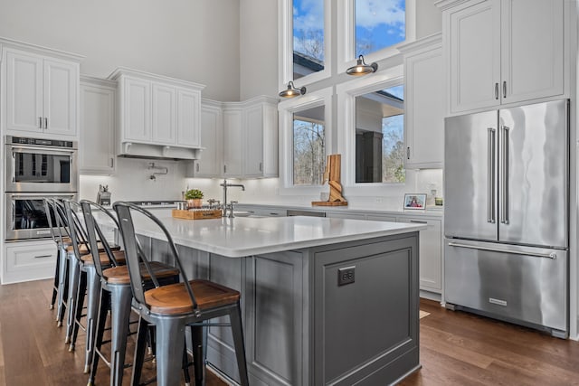 kitchen featuring a kitchen island with sink, stainless steel appliances, a towering ceiling, light countertops, and decorative backsplash