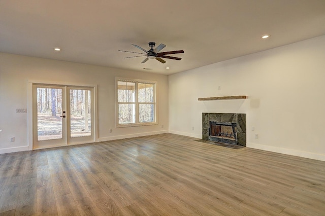 unfurnished living room with a tiled fireplace, wood-type flooring, and ceiling fan