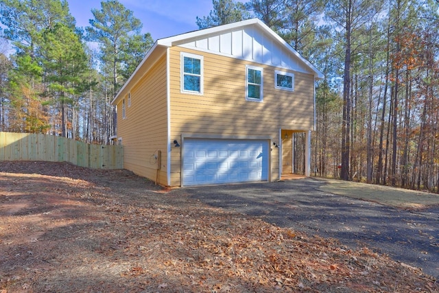 view of home's exterior with aphalt driveway, board and batten siding, an attached garage, and fence