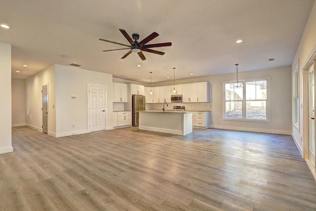 unfurnished living room featuring ceiling fan with notable chandelier, sink, and light hardwood / wood-style floors