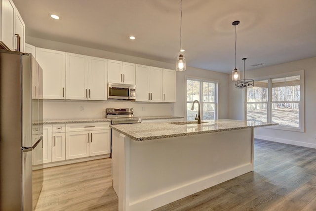 kitchen featuring pendant lighting, sink, white cabinetry, stainless steel appliances, and a center island with sink