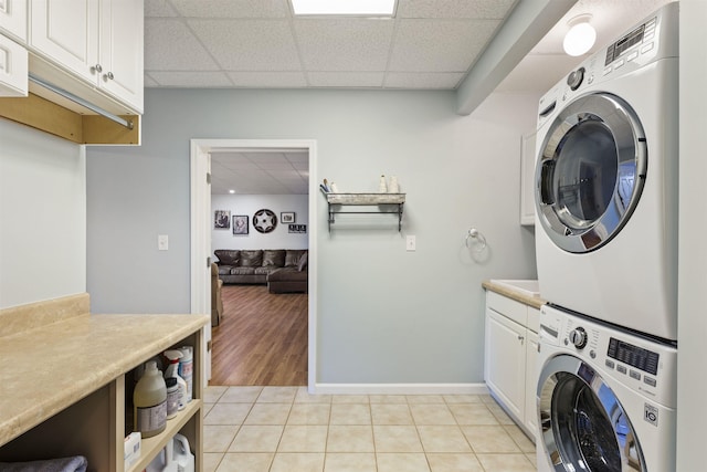 laundry area with cabinet space, light tile patterned floors, baseboards, and stacked washer and clothes dryer