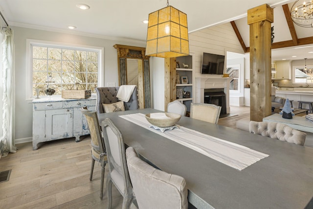 dining space featuring a notable chandelier, a fireplace, lofted ceiling, light wood-style floors, and ornamental molding