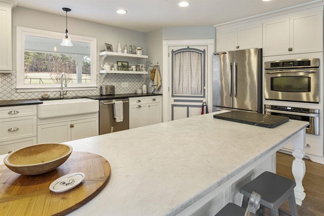 kitchen with white cabinets, a sink, stainless steel appliances, pendant lighting, and backsplash