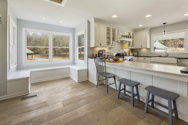 kitchen featuring range, custom exhaust hood, light wood-style floors, a kitchen bar, and a sink