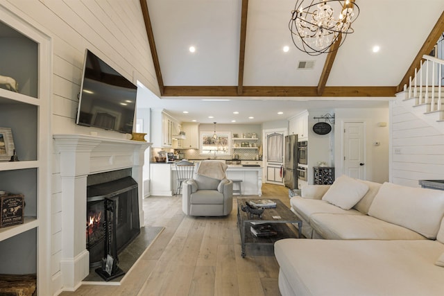 living area featuring a warm lit fireplace, visible vents, beamed ceiling, stairs, and light wood-style floors