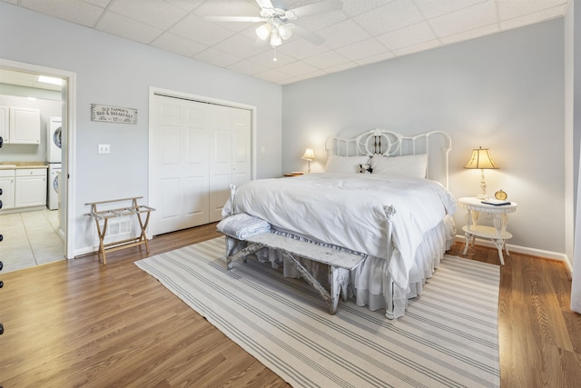 bedroom with a paneled ceiling, baseboards, a closet, stacked washing maching and dryer, and light wood finished floors